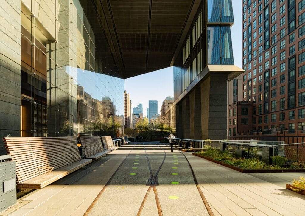 En panoramisk udsigt af en businesspark med glasbygninger, bænke langs en gangsti og sporlinjer. I baggrunden kan man se byens skyline og grønne områder.